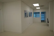 Thumbnail for Empty office hallway with white walls, framed photos, fluorescent ceiling lights, and a window at the end.