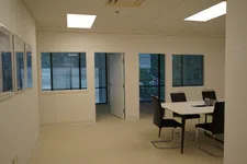 Thumbnail for Bright, empty office room with beige carpet, white walls, table with black chairs, and windows showing outdoor greenery.