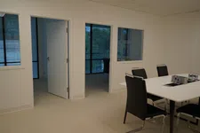 Thumbnail for Modern office room with white walls, black chairs around a table, and open doors showing adjacent rooms.