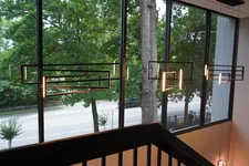 Thumbnail for Modern geometric pendant lights hanging in front of large windows overlooking a tree-lined street.