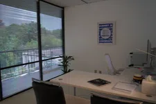 Thumbnail for Modern office with large window blinds, white desk, black chair, and a green plant by the window.