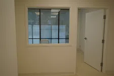 Thumbnail for Empty office space with a glass window showing a chair and an open door leading to another room.