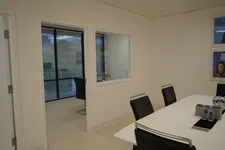 Thumbnail for Modern office meeting room with black chairs, white table, water bottles, and glass window to adjacent room.