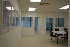 Thumbnail for Bright office space with white walls, framed pictures, windows, and a small meeting area with black chairs and table.