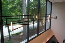 Thumbnail for Modern geometric pendant lights hanging in front of large windows overlooking a tree-lined street.