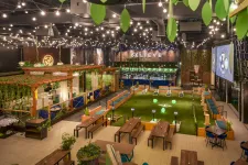 Thumbnail for Indoor recreational area with bocce courts, seating, greenery, string lights, and a large BELIEVE sign on the back wall.