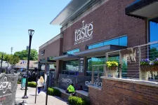 Thumbnail for Taste Wine Bar and Market exterior with outdoor seating, brick facade, and flower planters under clear blue sky.