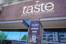 Thumbnail for Taste Wine Bar and Market storefront with a Spring 2026 event banner on a brick building under blue sky.