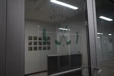 Thumbnail for Glass door with Elite Fit Golf logo featuring crossed golf clubs and laurel branches in a dimly lit hallway.
