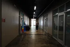 Thumbnail for Dimly lit hallway in an office building with a woman walking towards an exit door at the end.