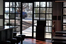 Thumbnail for Interior view of a cafe with stools and tables near large glass windows showing an outdoor sidewalk and passing car.