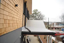 Thumbnail for Modern building exterior with wooden siding, flat white roof, black gutters, and urban street view in background