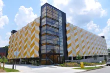 Thumbnail for Modern office building with geometric yellow and white patterned facade and glass stairwell under a blue sky.