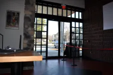 Thumbnail for Interior view of a glass door entrance with stone and brick walls and a red rope barrier inside a building.