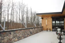 Thumbnail for Outdoor stone patio with metal railings and wooden building siding beside bare trees under an overcast sky.