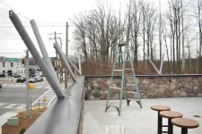 Thumbnail for Outdoor patio under construction with metal poles, a green ladder, stone wall, and wood stools on a concrete floor.