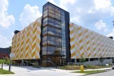 Thumbnail for Modern parking garage with geometric yellow and white exterior panels and glass elevator shaft under a blue sky.