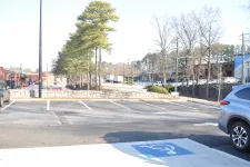 Thumbnail for Empty parking lot with a few cars, trees, and buildings in a sunny daytime setting.