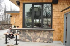 Thumbnail for Man working on outdoor seating area with stone and wood siding during construction or renovation.