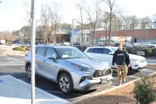Thumbnail for Man walking near silver Toyota SUV parked in outdoor lot with another white SUV and stop sign in background
