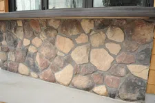 Thumbnail for Rustic stone wall facade with various shades of brown and gray stones under a wooden ledge.