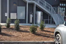 Thumbnail for Small bushes planted in mulch bed beside building with utility boxes, stairs, and a parked silver car.