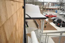 Thumbnail for View down a staircase alongside a wooden shingle wall overlooking a parking lot with trucks and buildings in the background.