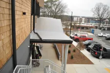 Thumbnail for View of modern building exterior with metal awning, staircase, parked trucks, and urban surroundings on a cloudy day