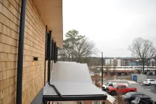 Thumbnail for Modern building exterior with wood siding, sloped gray metal awnings, and a parking lot with vehicles and trees in the background