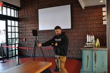Thumbnail for Man adjusting a tripod-mounted device in a modern room with brick walls and large windows.
