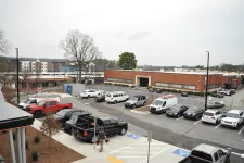 Thumbnail for Urban parking lot with various vehicles, including trucks and vans, in front of a brick commercial building on a cloudy day.