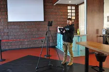 Thumbnail for Man in casual clothes operating tablet connected to tripod camera setup in modern indoor space with brick wall.
