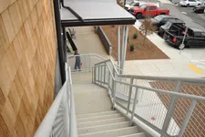 Thumbnail for Outdoor concrete staircase with metal railing leading down beside wood-paneled building near parking lot with trucks.