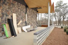 Thumbnail for Outdoor stone wall patio with wooden roof and construction materials stacked along the wall during renovation.