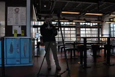 Thumbnail for Man using camera tripod to record or photograph inside a dimly lit, modern industrial-style restaurant or cafe.