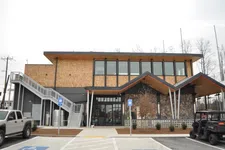 Thumbnail for Modern two-story building with wooden accents, large windows, external staircase, and parked vehicles in front.