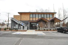 Thumbnail for Modern two-story building with stone facade, wooden accents, angular roof, and adjacent parking with handicap spaces.