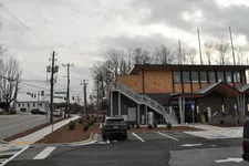 Thumbnail for Modern two-story building with exterior staircase in parking lot under cloudy sky near a street intersection.