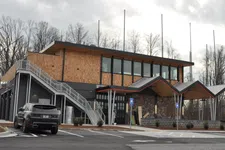 Thumbnail for Modern two-story building with wooden and stone facade, large windows, and outdoor stairway under cloudy sky.