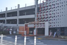 Thumbnail for Multi-level parking garage entrance with a white and orange facade and parking barriers on a sunny day.