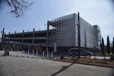 Thumbnail for Modern multi-level parking garage with white perforated facade and a car parked outside on a sunny day
