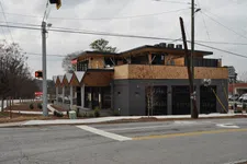 Thumbnail for Modern two-story building with wooden accents and large windows on a cloudy day at a street corner.