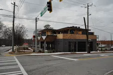 Thumbnail for Modern two-story commercial building with wood accents at a city intersection on a cloudy day