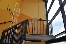 Thumbnail for Stairwell leading to Level 6 with yellow walls, black railings, and large windows showing blue sky and clouds.