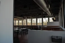Thumbnail for Empty modern restaurant dining area with large windows, high ceilings, and brown leather booths during daytime.