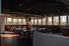 Thumbnail for Empty modern cafeteria with long tables, benches, large windows, and exposed ceiling pipes in natural light.