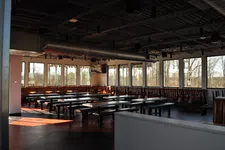Thumbnail for Empty modern cafeteria with long tables, benches, large windows, and exposed ceiling ducts in daylight.