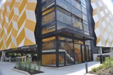 Thumbnail for Modern parking garage with yellow and white geometric patterned facade and glass-enclosed staircase.