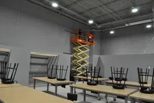 Thumbnail for Scissor lift elevating two workers inside a large industrial room with tables and chairs stacked upside down.
