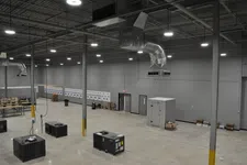 Thumbnail for Spacious empty industrial warehouse with concrete floor, large HVAC units, and gray walls under bright ceiling lights.
